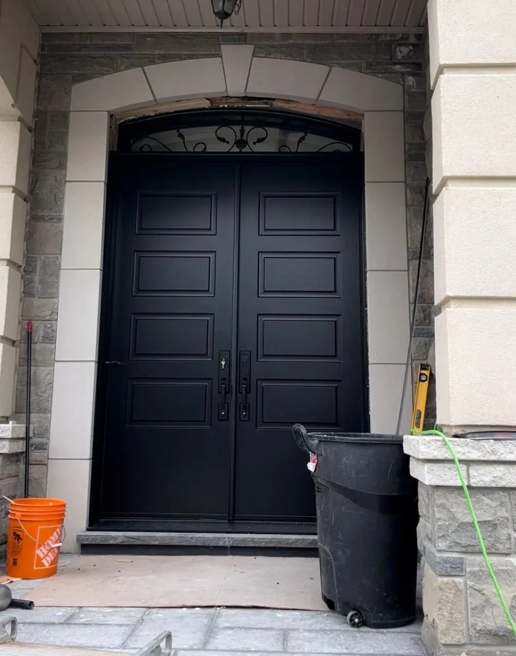 Matte black double entry doors with decorative transom on a stone Aurora entrance